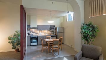 A modern kitchen with a dining area, a large plant, and a grey armchair.
