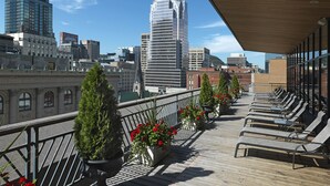 A balcony with lounge chairs and potted plants, overlooking a cityscape with modern buildings. - Le Square Phillips Hotel And Suites (Montreal)