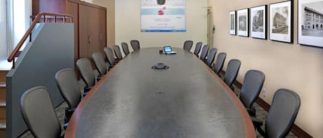 A conference room with a long table, chairs, a laptop, and a mounted screen displaying a webpage.