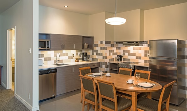 A modern kitchen with a dining area, featuring a stainless steel refrigerator, microwave, and stove, with a checkered tile backsplash. - Le Square Phillips Hotel And Suites (Montreal)