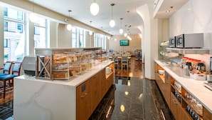 A modern cafe with a marble counter, wooden chairs, and a TV screen. - Le Square Phillips Hotel And Suites (Montreal)