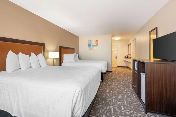 A hotel room with two beds, a desk, a television, and a bathroom in the background.