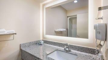 A bathroom with a granite countertop sink, a mirror, a towel rack, and a shower visible in the reflection.
