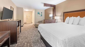 A hotel room with a large bed, a desk with a flat-screen TV, a chair, a desk lamp, and a painting on the wall.