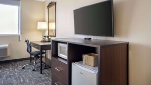 A hotel room with a desk, chair, flat-screen TV, microwave, mini-fridge, and a large mirror.