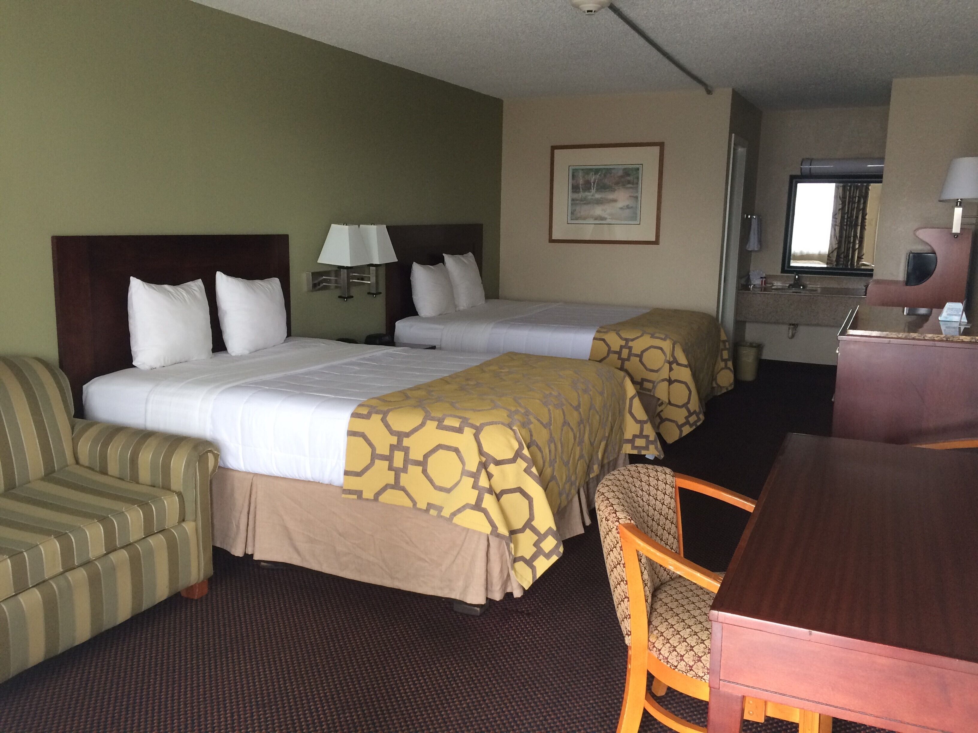 Een hotelkamer met twee bedden, een bureau, een stoel, een lamp en een schilderij aan de muur.