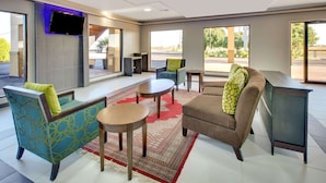 Un moderno vestíbulo de hotel con un sofá, un sillón y una mesa de centro, un televisor de pantalla plana montado en la pared y grandes ventanas que ofrecen vistas al exterior.