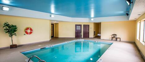 A large indoor swimming pool with clear lane markings, a lifebuoy on the wall, and a potted plant.