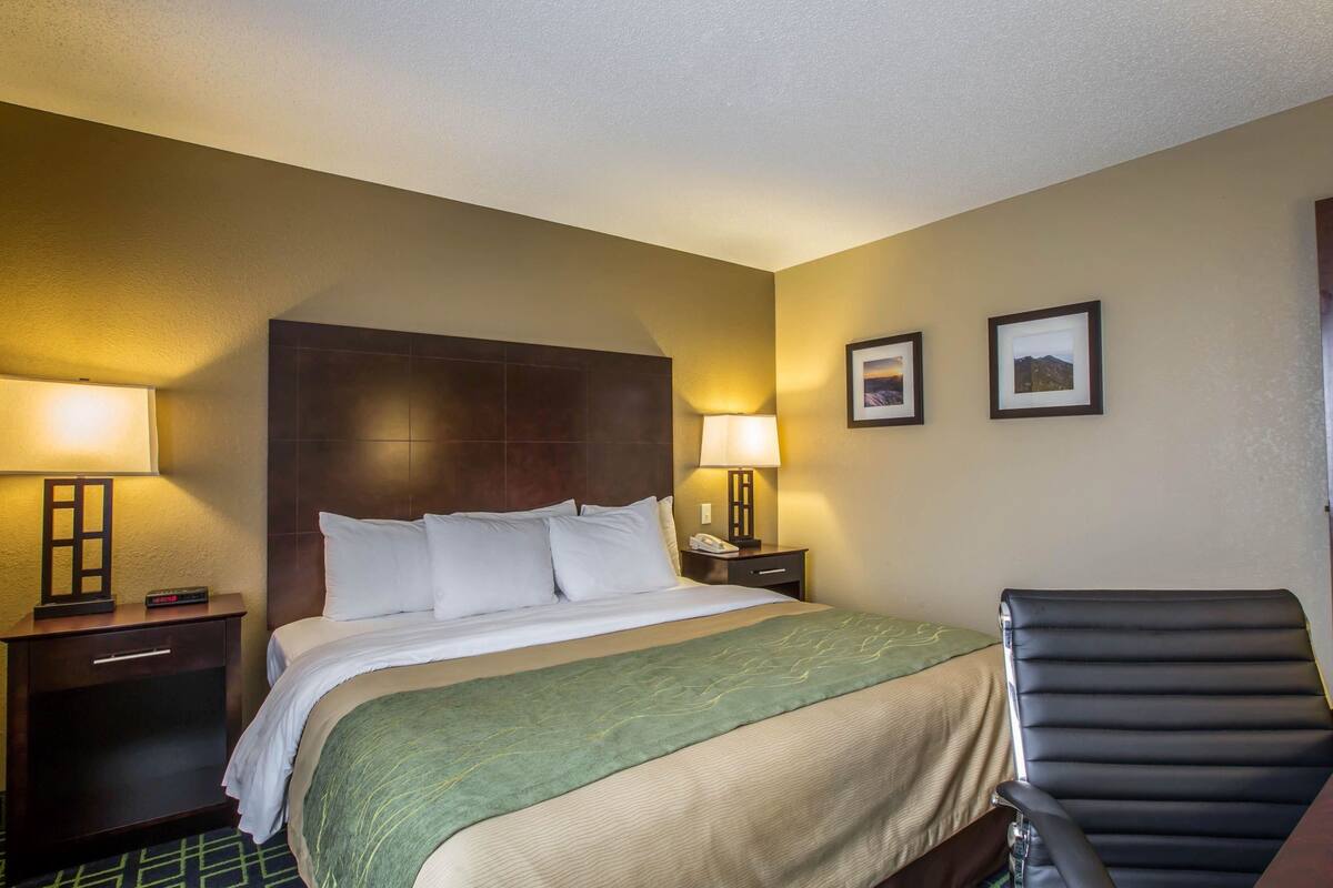 A hotel room with a large bed, two bedside lamps, a nightstand, a chair, and two framed pictures on the wall.