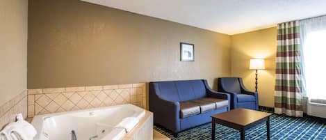 A hotel room with a large bathtub, a sofa, a chair, and a small table.