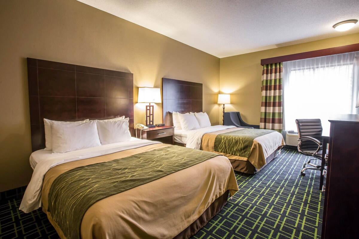 A hotel room with two beds, a desk, a chair, and a window with curtains.