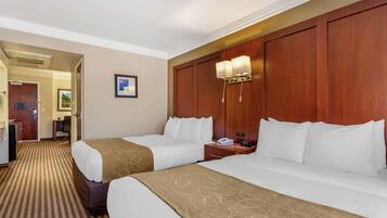 A hotel room with two beds, a wooden headboard, a bedside table with a lamp, and a framed picture on the wall.