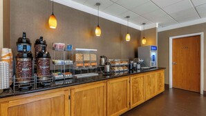 A hotel breakfast area with a coffee station, a self-serve beverage station, and a food display.