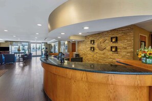 A reception area with a curved wooden counter, a stone wall with framed pictures, and a reception desk with a clock. - Comfort Suites Visalia Convention Center (Visalia)