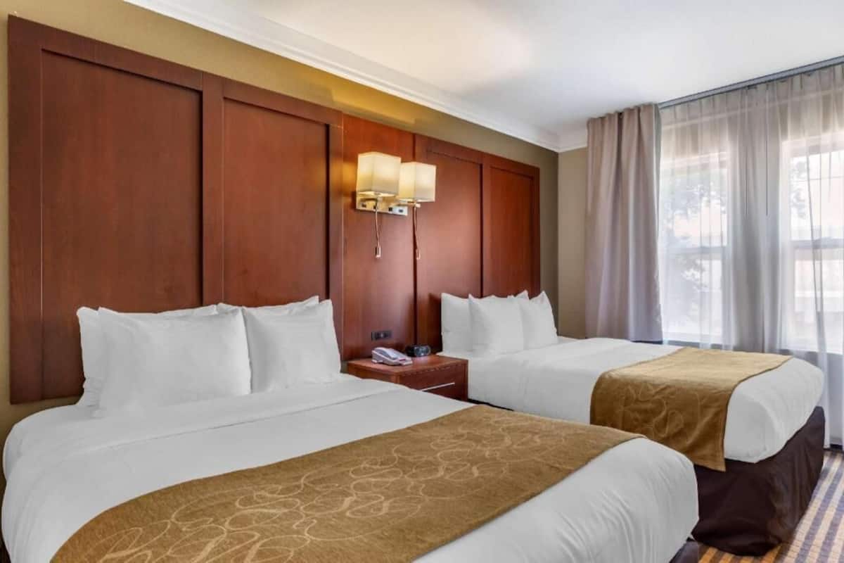 Ein Hotelzimmer mit zwei Betten, einem hölzernen Kopfteil, einem Nachttisch mit Lampe und einem fenster mit Vorhängen.