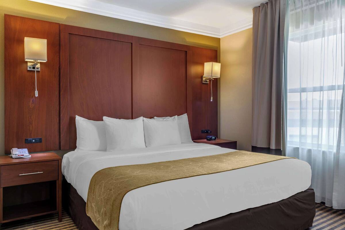 Ein Hotelzimmer mit einem großen Bett, zwei Nachttischen, einer Lampe und einem Fenster mit Vorhängen.