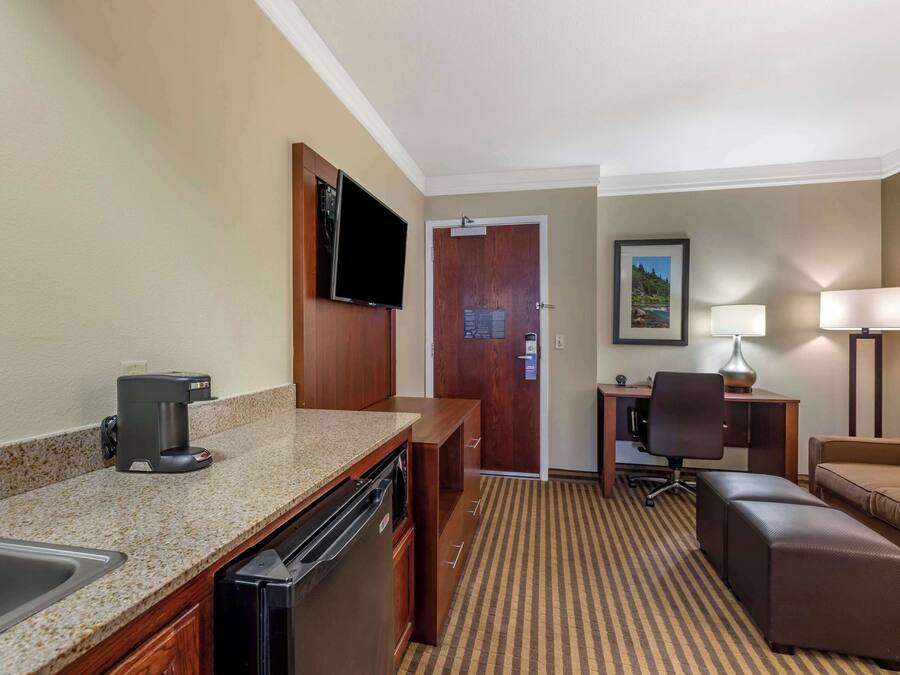 A hotel room with a kitchenette, a dining area, a sofa, and a TV.