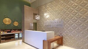 A reception desk with a sign for Wynham Garden Hotel, a patterned wall, and a display of snacks. - Wyndham Garden Monterrey Valle Real (Monterrey)