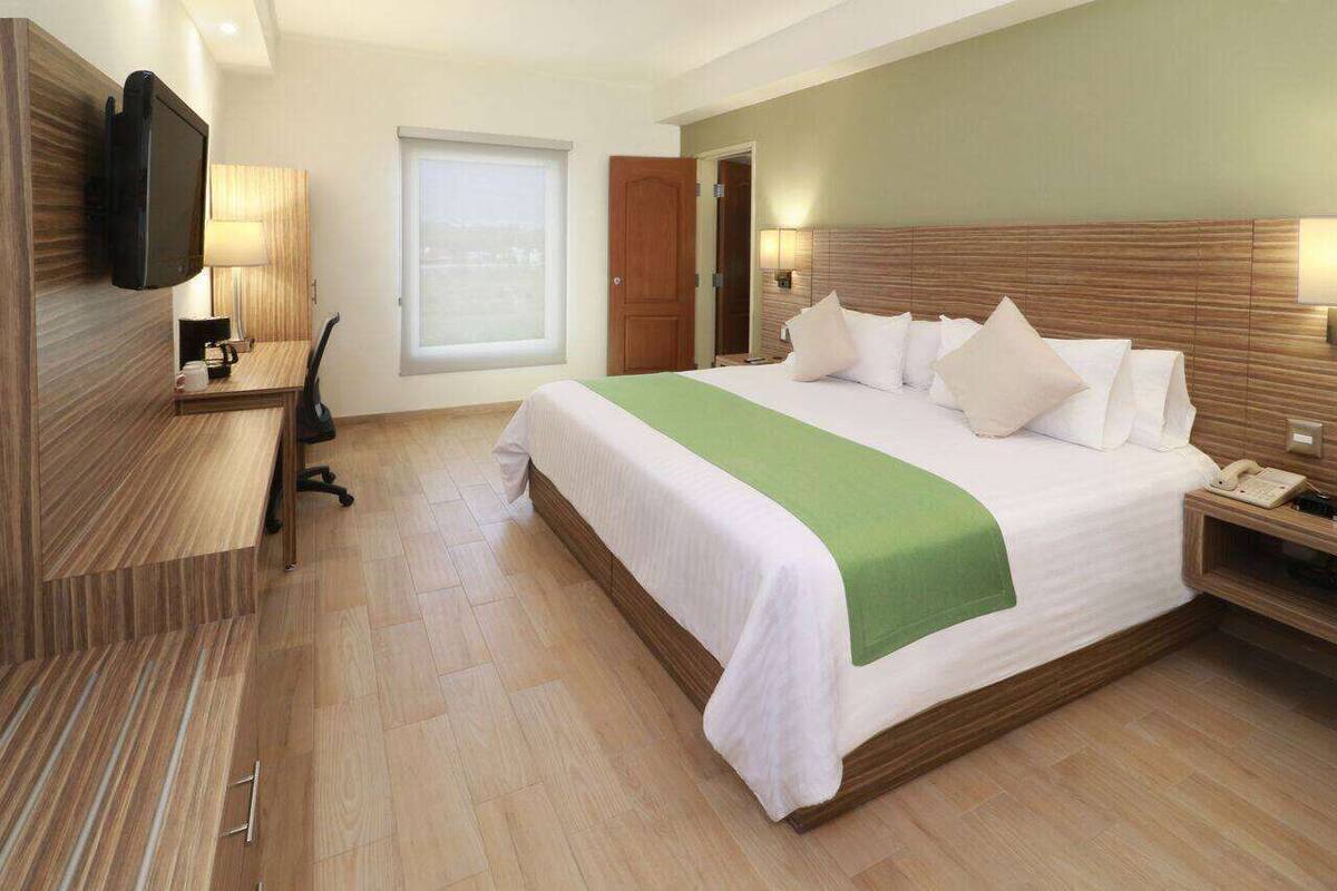 Ein Hotelzimmer mit einem großen Bett, Nachttischen, einem Schreibtisch, einem Sessel und einem Fernseher sowie einem Fenster.