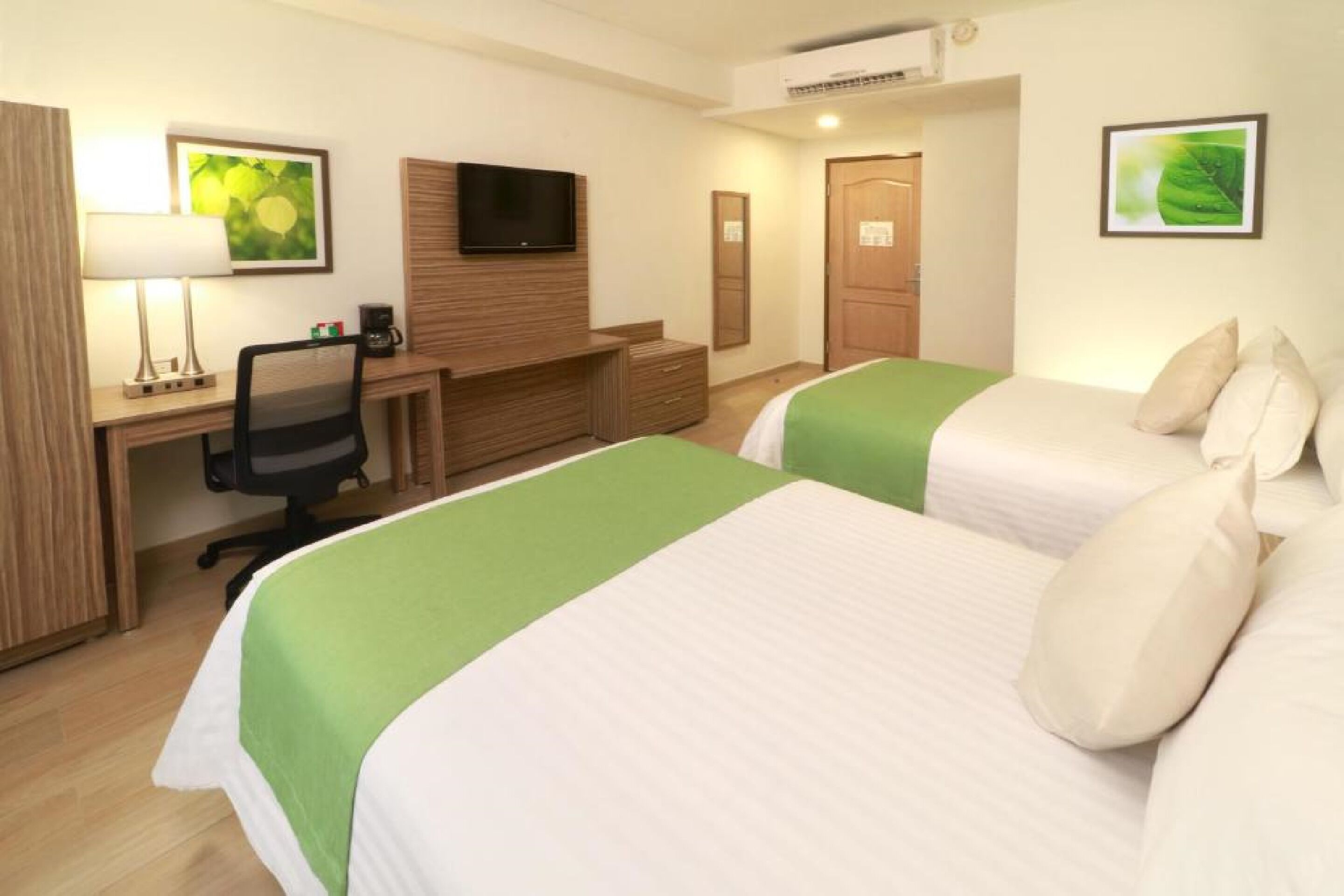 Une chambre d’hôtel avec deux lits, un bureau avec une chaise, une télévision et une armoire en bois.