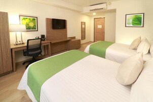 A hotel room with two beds, a desk with a chair, a TV, and a wooden wardrobe.