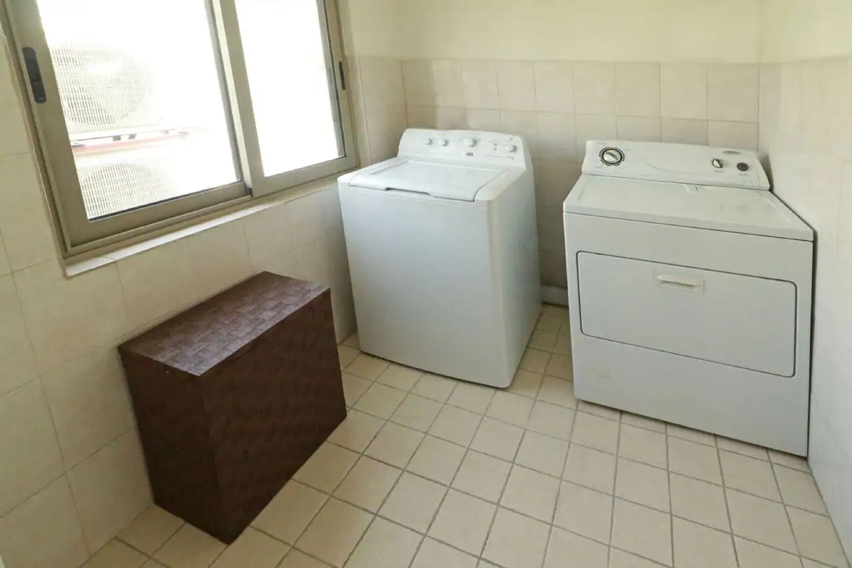 A laundry room with two washing machines and a wooden bench.