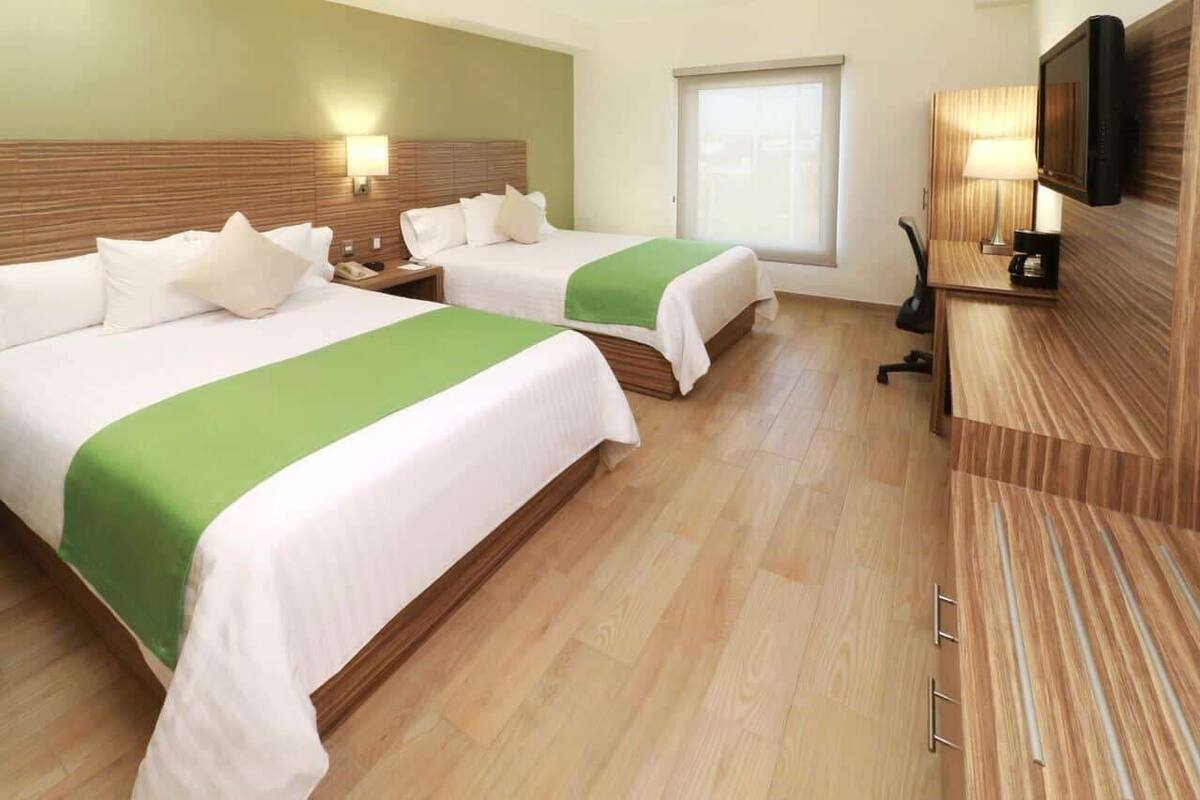 Ein Hotelzimmer mit zwei Betten, einem Schreibtisch, einem Fernseher und einem Fenster.