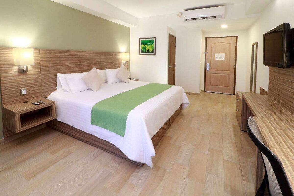 Ein Hotelzimmer mit Bett, Nachttisch, Lampe, Fernseher und einer Tür.