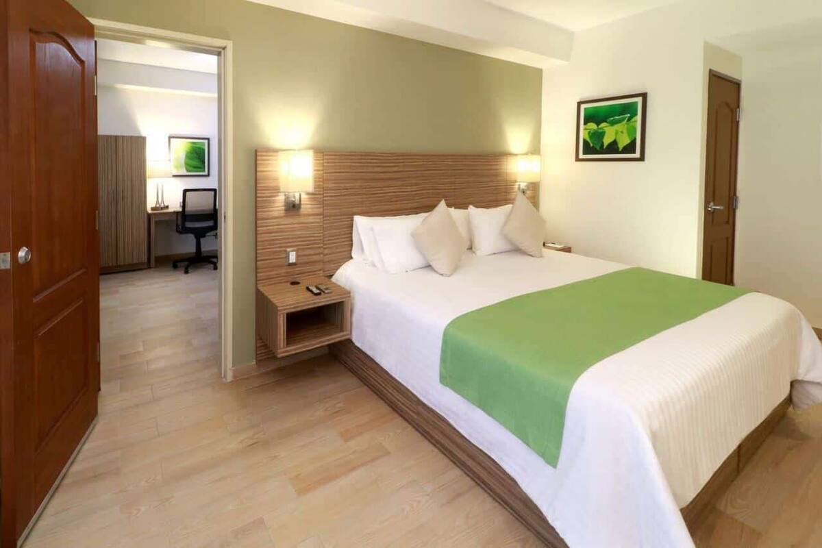 Ein Hotelzimmer mit einem großen Bett, einem Holzkopfende, Nachttischen, einem Schreibtisch und einem Sessel.