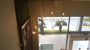 A modern interior with a seating area, a large window with a view of palm trees, and a sign for a hair salon. - Wyndham Garden Monterrey Valle Real (Monterrey)
