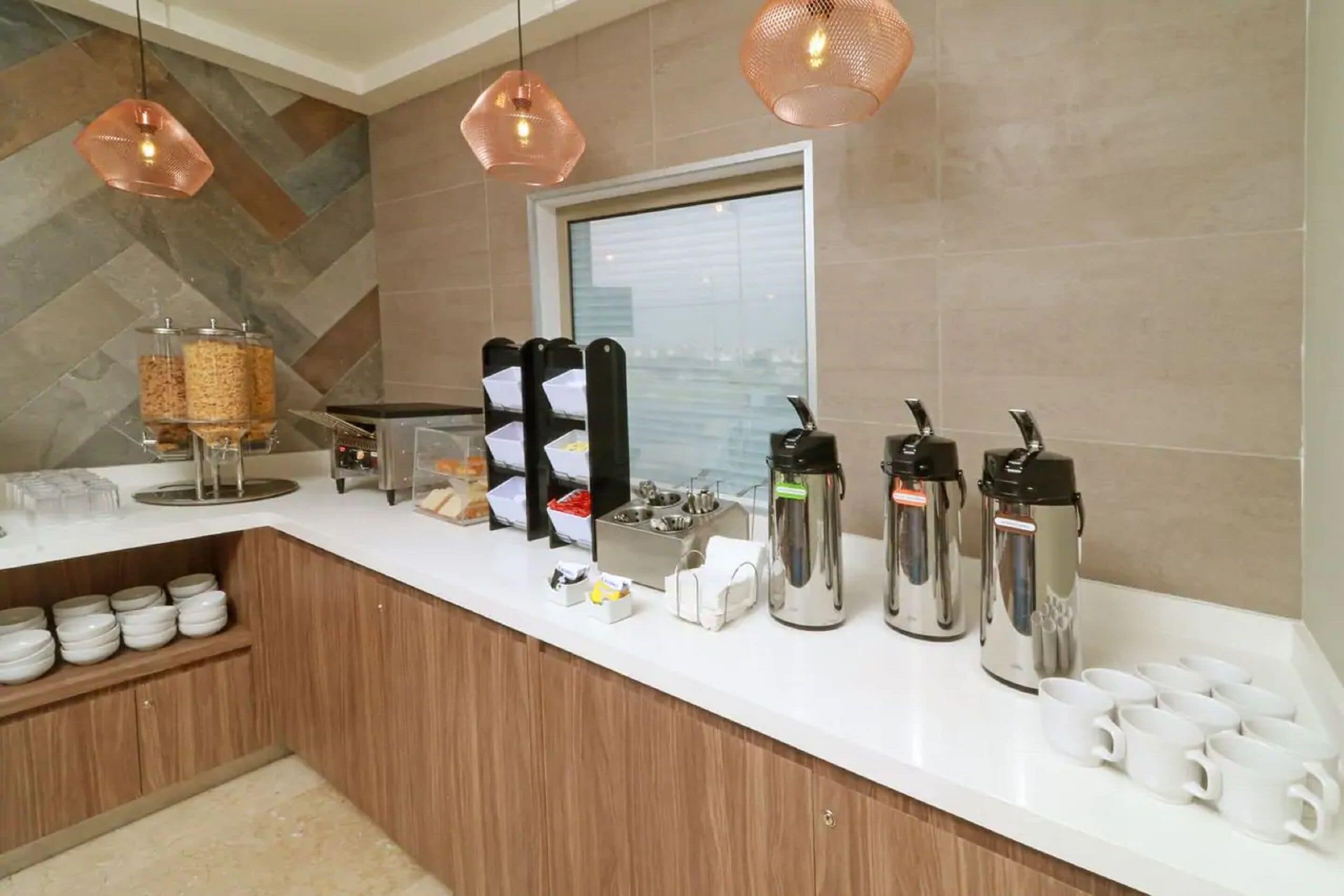 Una cocina moderna con encimera blanca, cafeteras y una ventana con persianas.