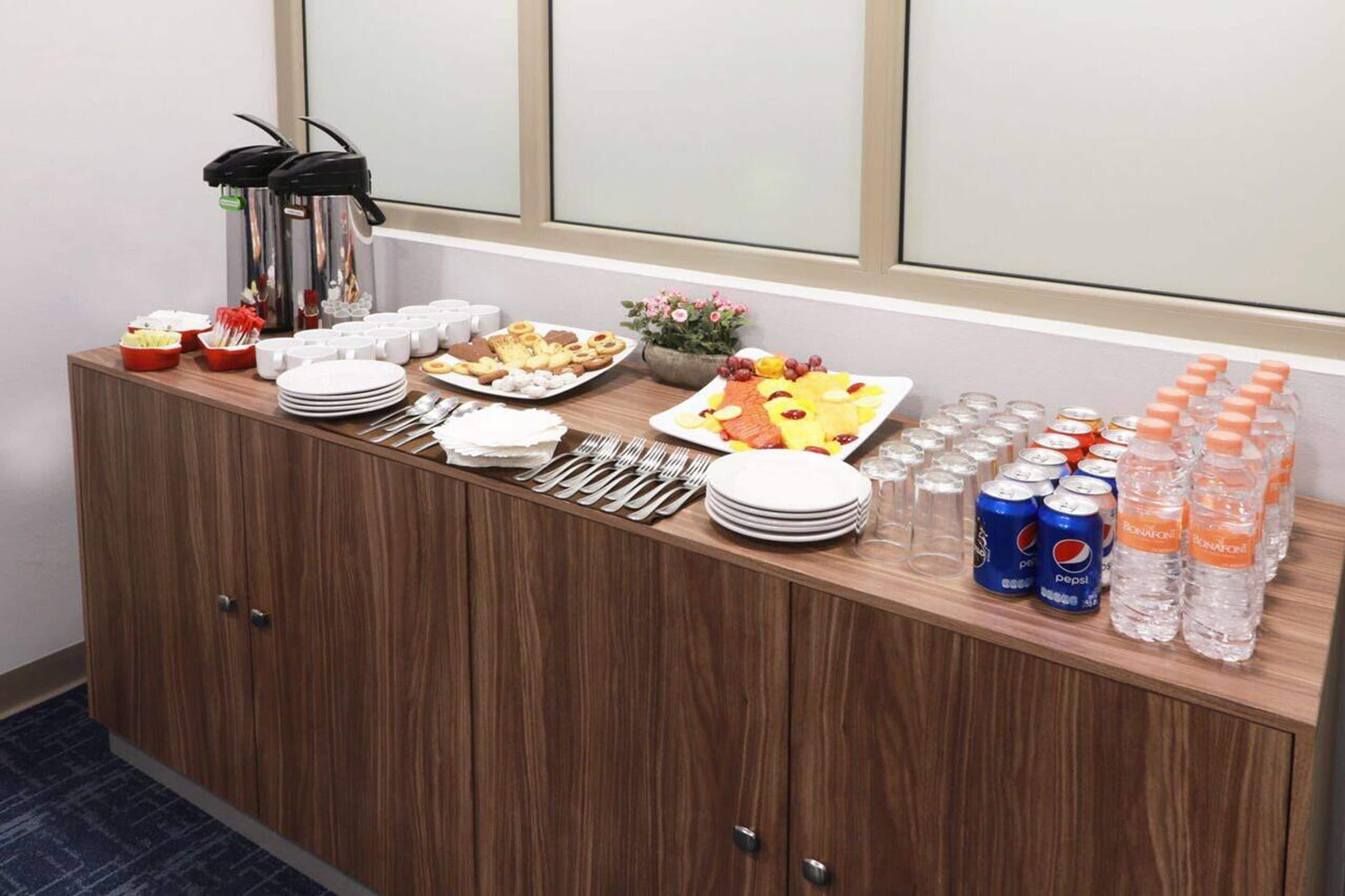 A buffet setup with various food items, plates, utensils, and bottled water.