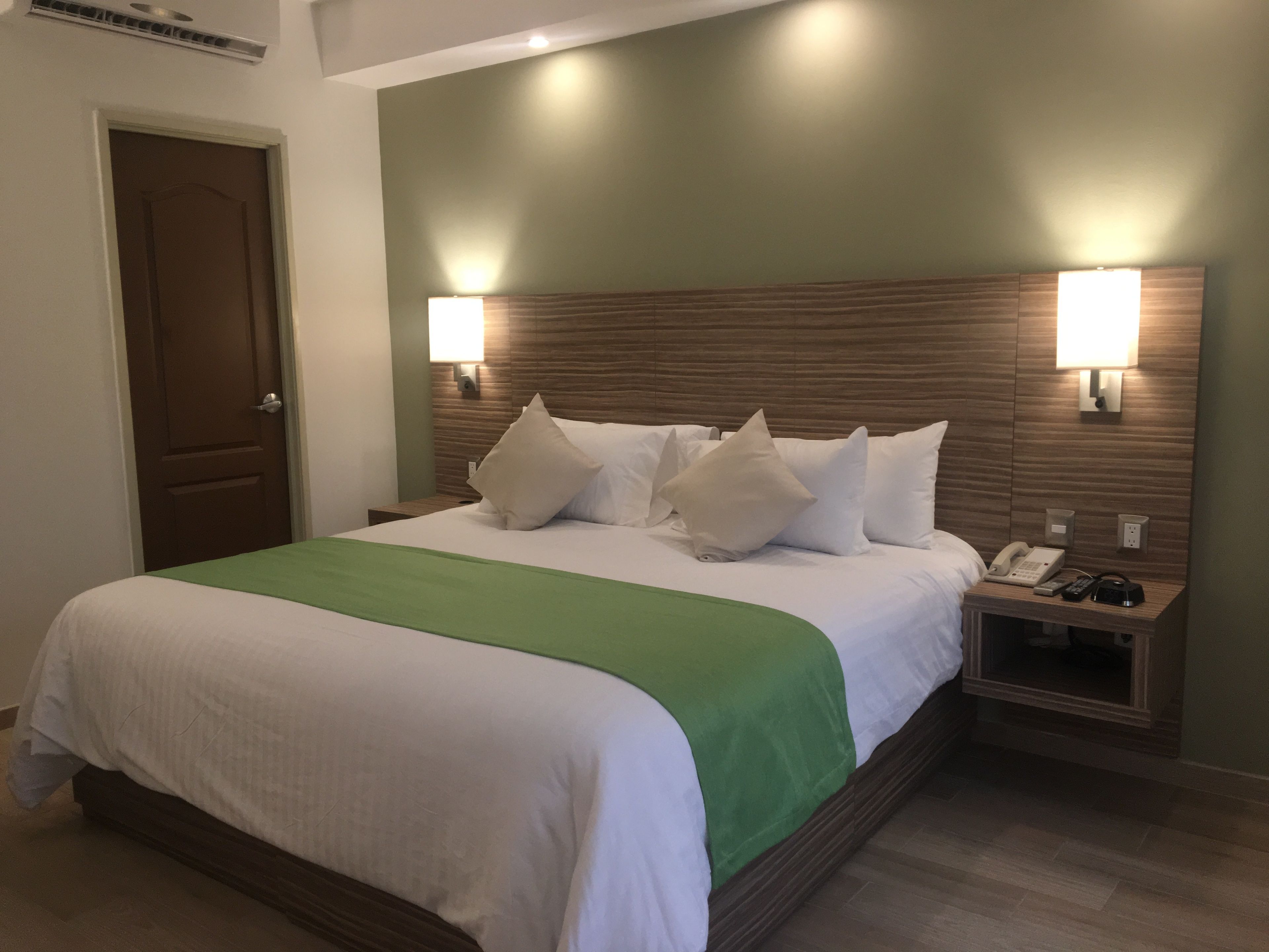 A hotel room with a large bed, two bedside tables, a nightstand, and a door.