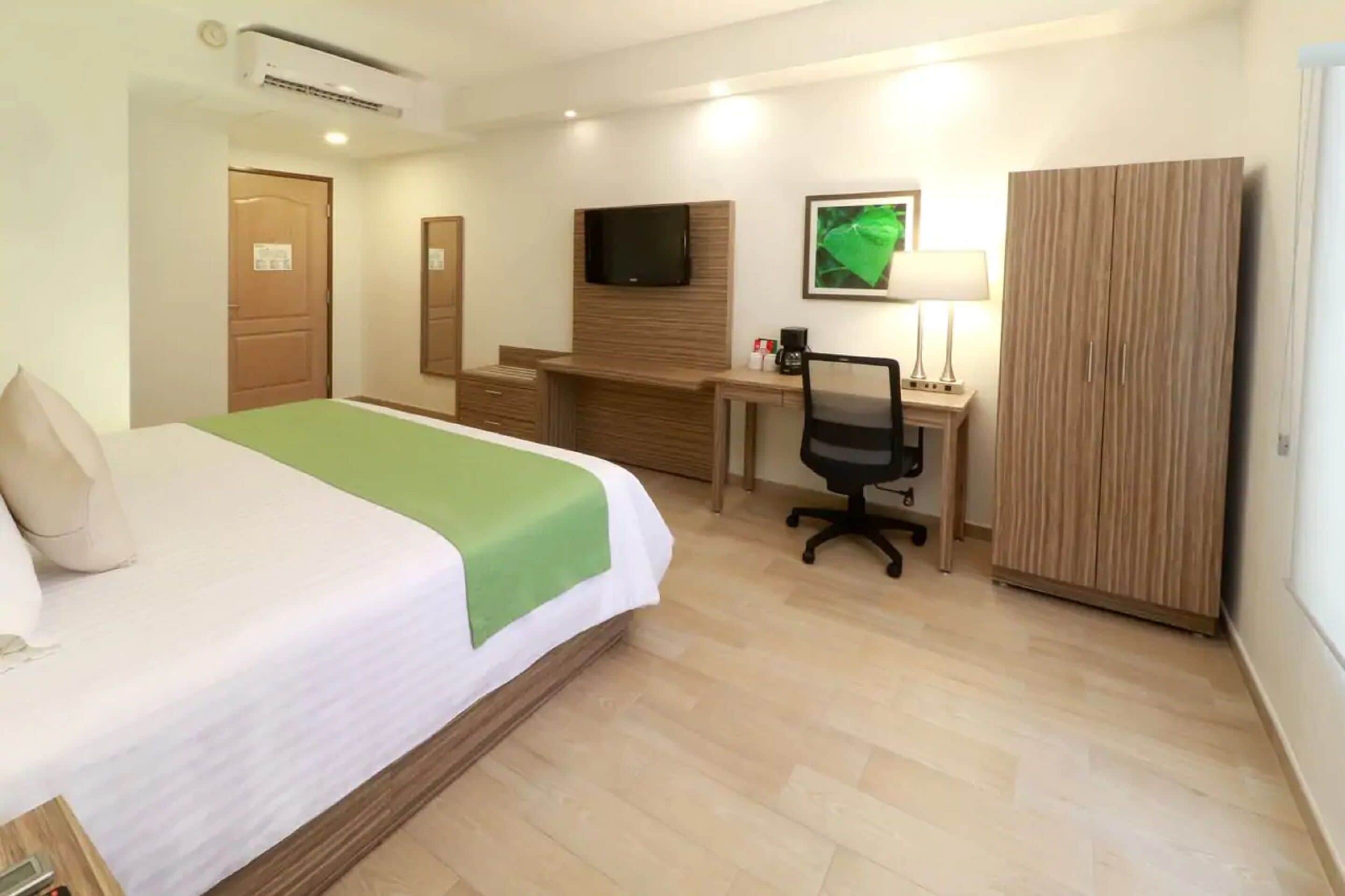 Una habitación de hotel con cama, escritorio, silla, televisor y armario.
