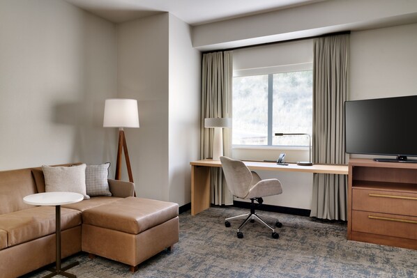 Habitación de hotel con sofá, escritorio, silla, televisor y lámpara.
