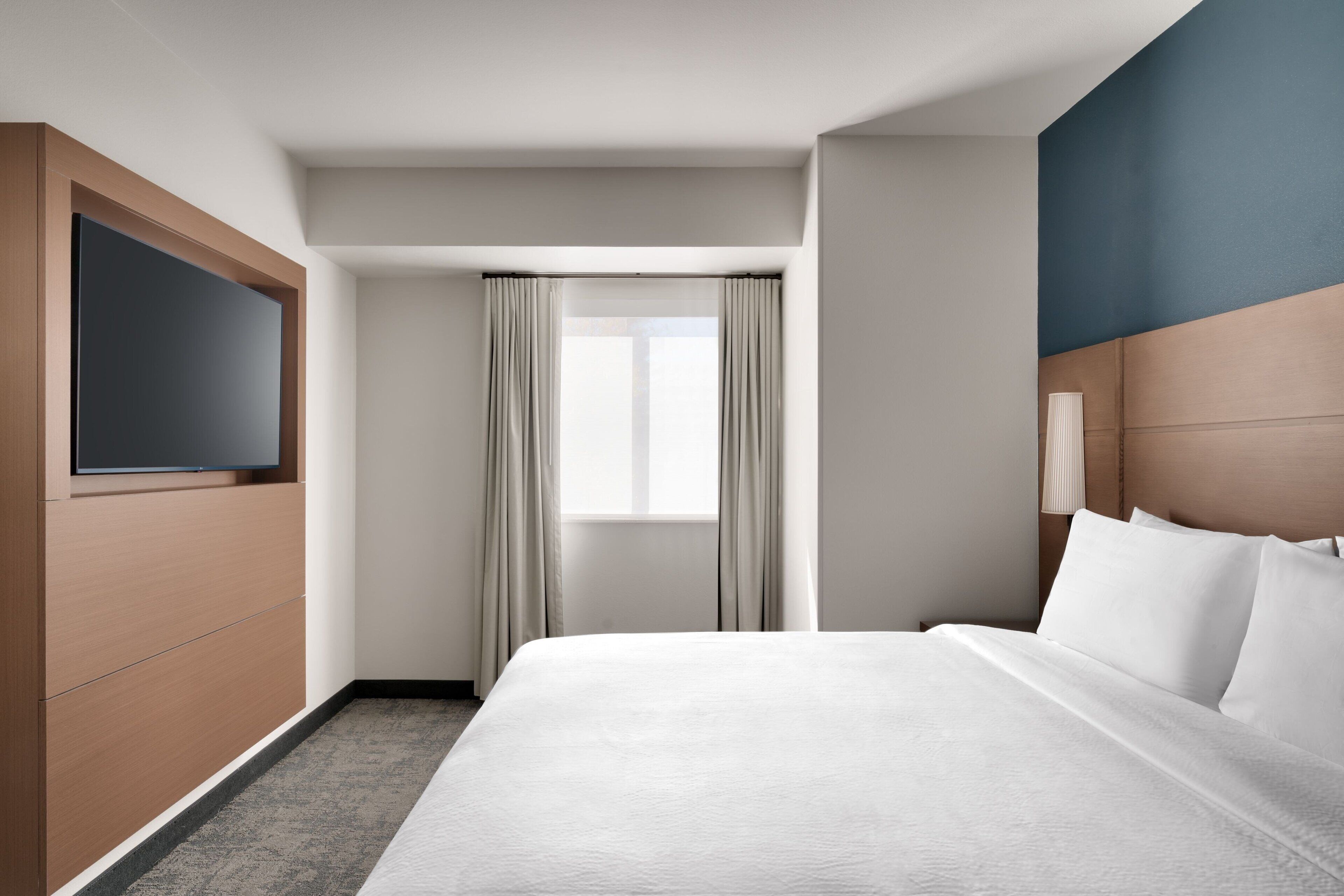 Habitació d'hotel amb un llit, televisió, finestra amb cortines i un capçal de llit.