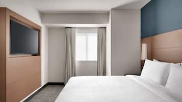 Ein Hotelzimmer mit Bett, Fernseher, Fenster mit Vorhängen und Kopfteil.