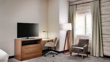 Habitación de hotel con cama, escritorio con televisor, silla, lámpara y ventana con cortinas.
