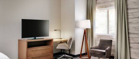 Une chambre d’hôtel avec un lit, un bureau avec une télévision, une chaise, une lampe et une fenêtre avec des rideaux.