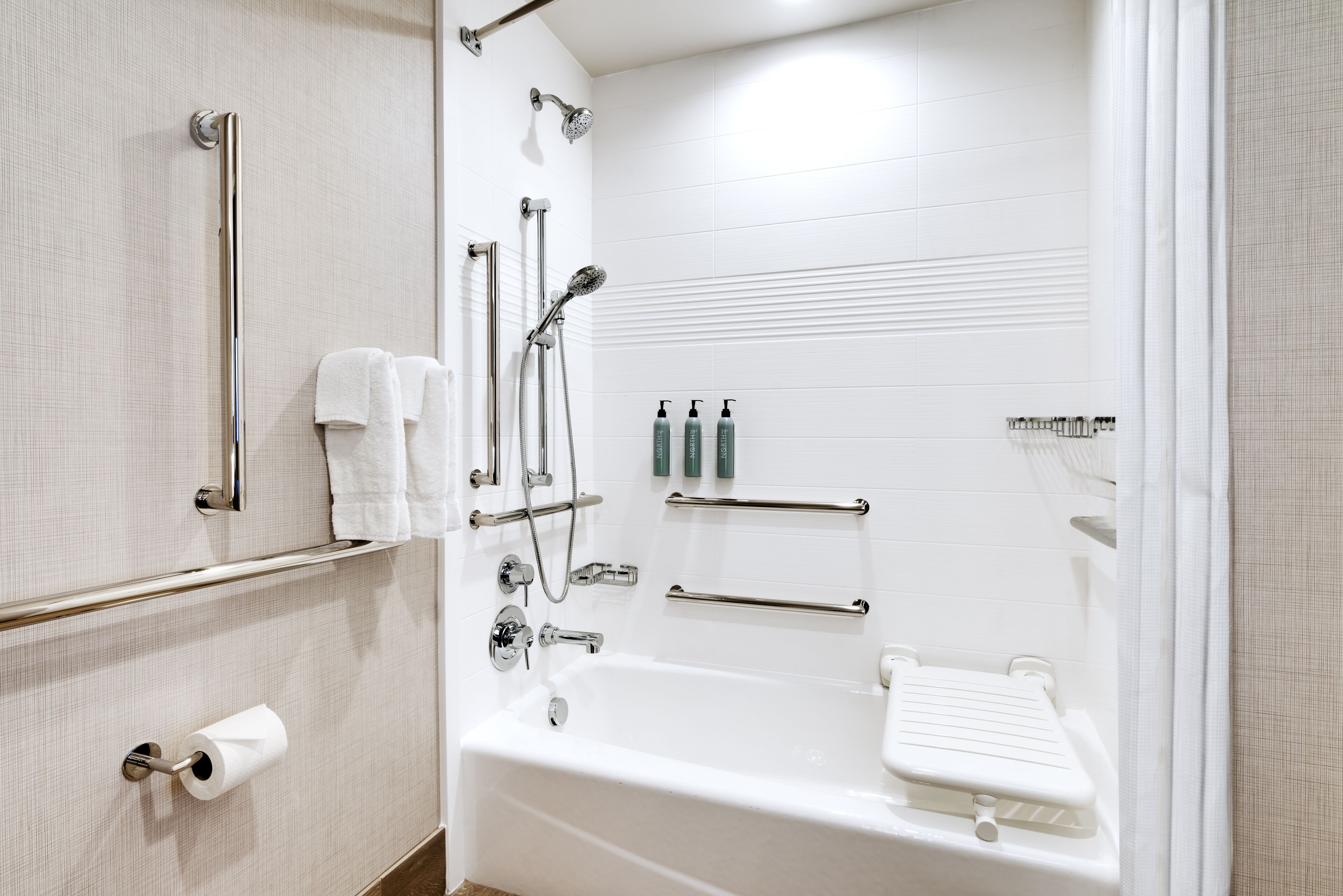 Een moderne badkamer met een bad, handgrepen, een toiletpapierhouder en toiletartikelen.