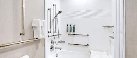 Un baño moderno con bañera, barras de apoyo, porta papel higiénico y artículos de aseo.
