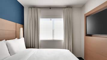Habitación de hotel con una cama grande, un televisor a la derecha y una ventana con cortinas.