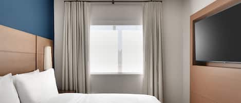 A hotel room with a large bed, a television on the right, and a window with curtains.