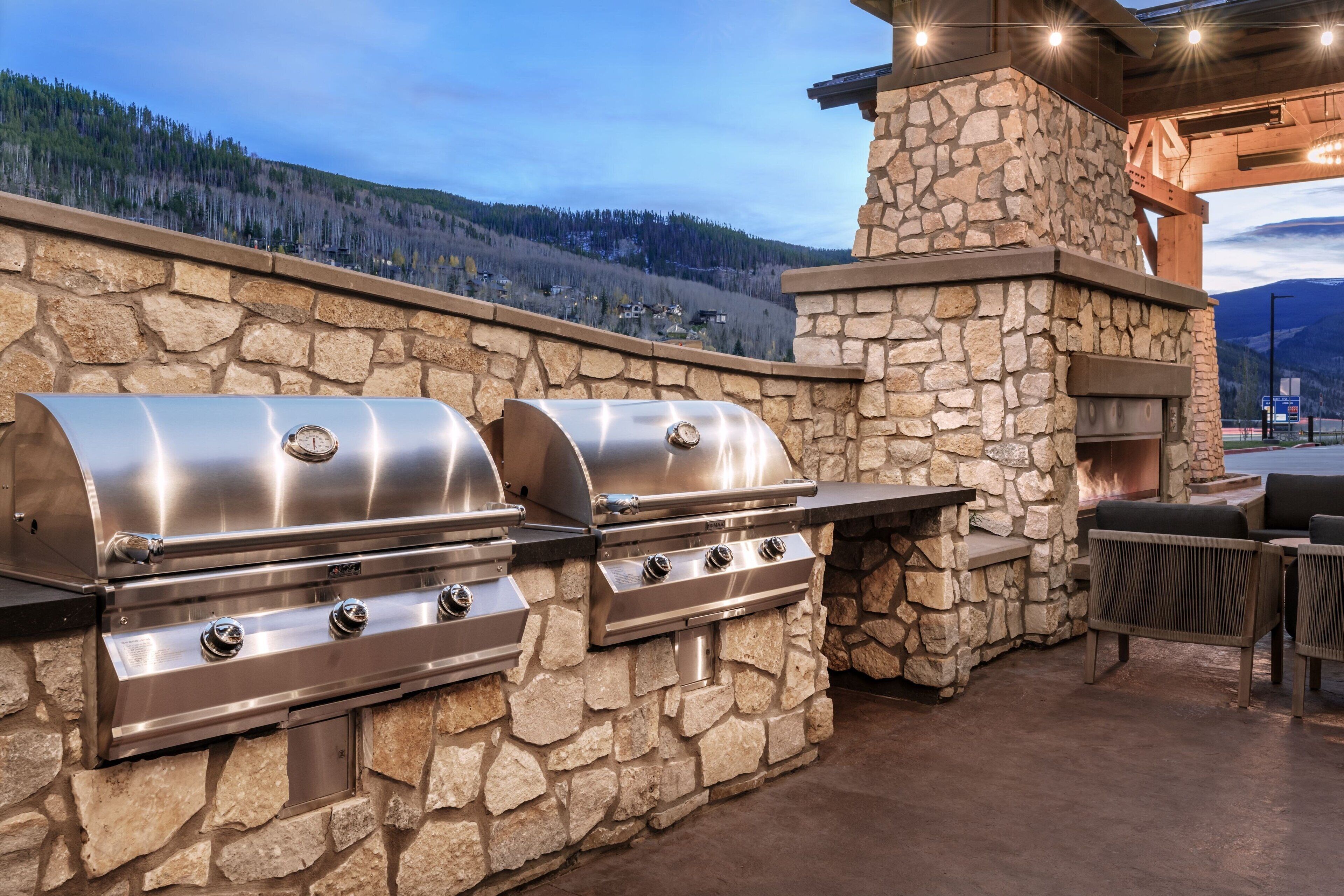 Cocina al aire libre de piedra con una parrilla y chimenea de piedra, con vistas a un paisaje montañoso.