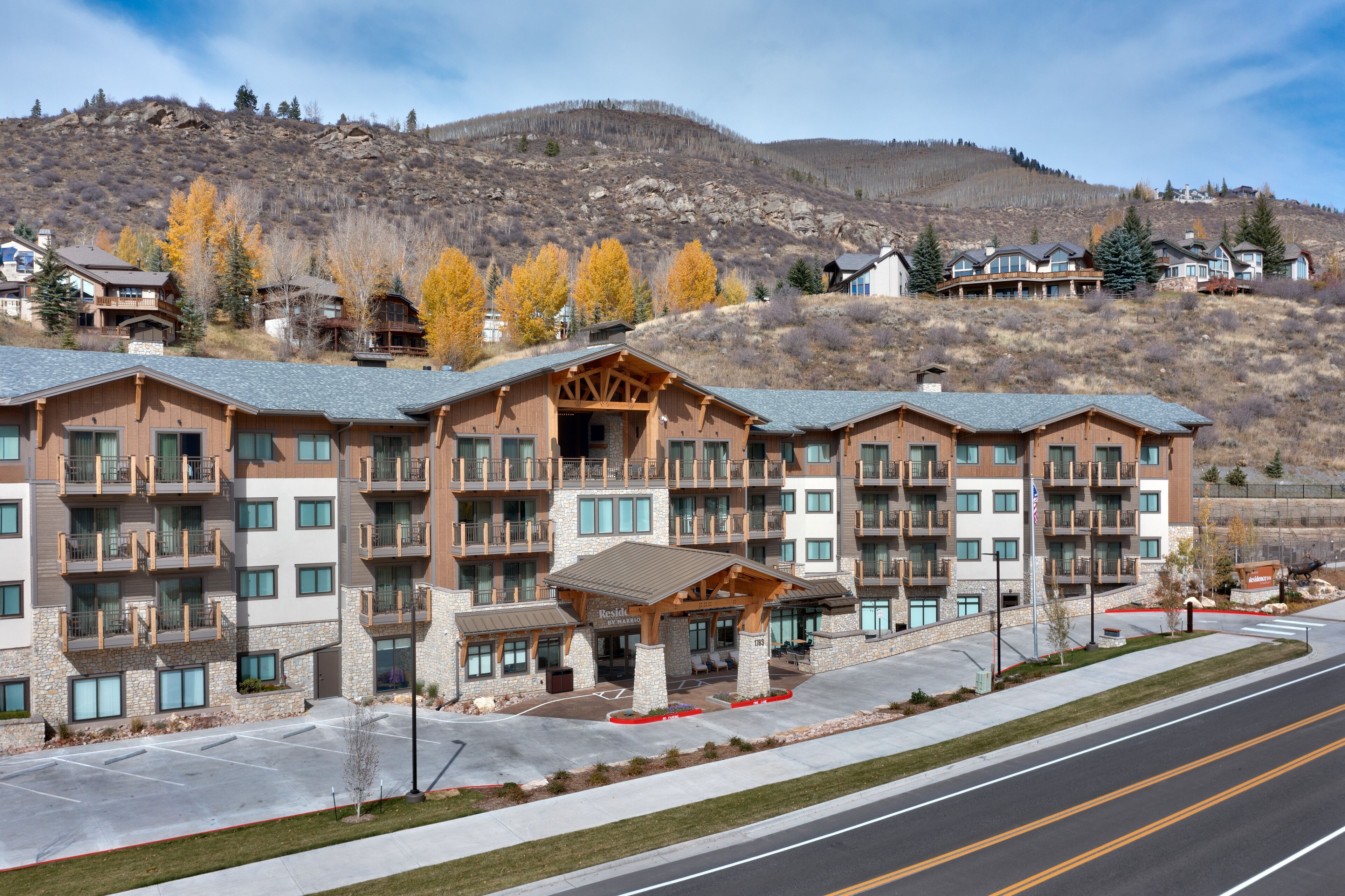 A multi-story hotel with balconies, a covered entrance, and a view of a mountainous landscape.