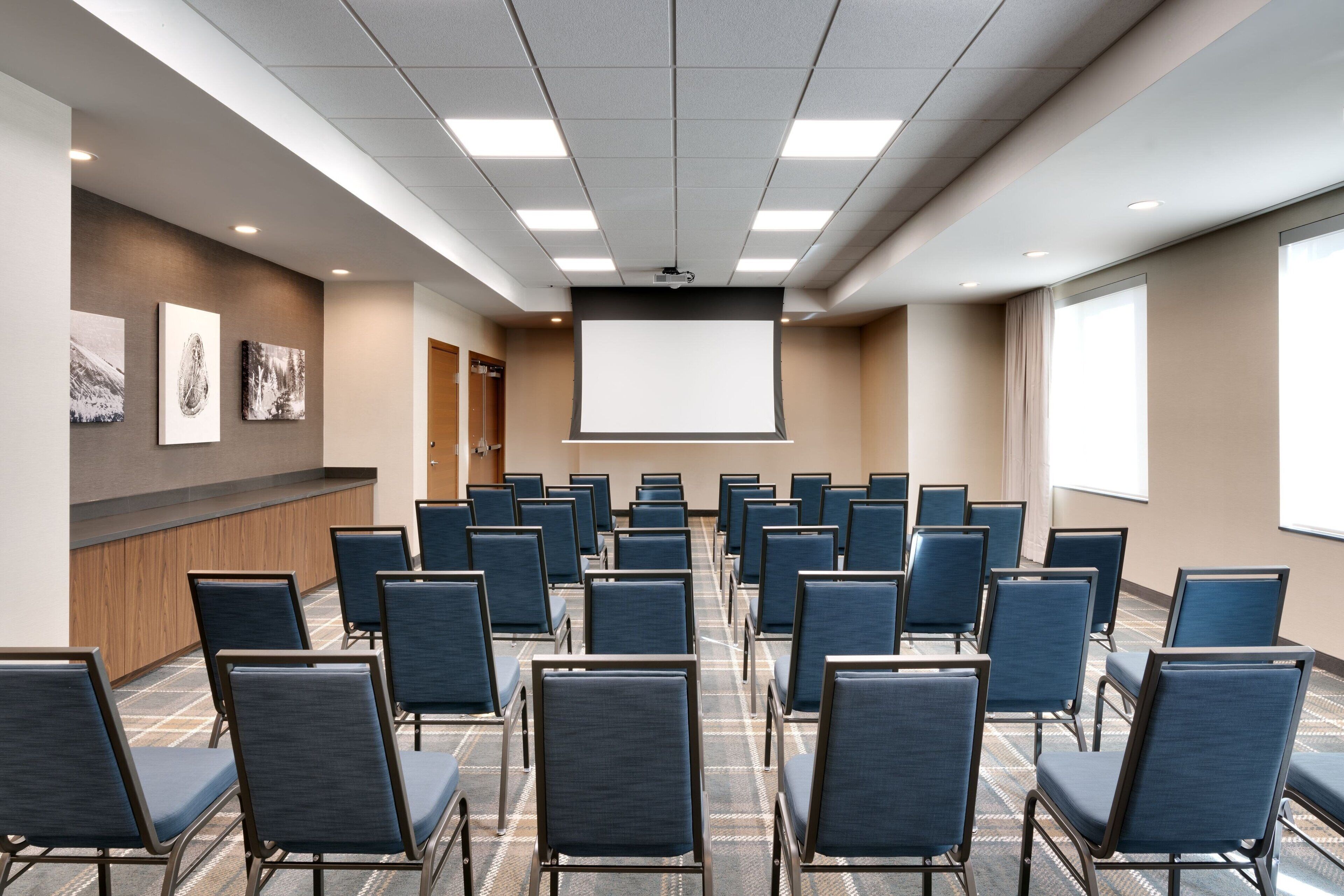 Un salón de conferencias con hileras de sillas, una pantalla de proyector y obras de arte en las paredes.