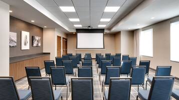 Un salón de conferencias con hileras de sillas, una pantalla de proyector y obras de arte en las paredes.