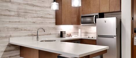 A modern kitchen with a marble backsplash, wooden cabinets, stainless steel appliances, and pendant lighting.