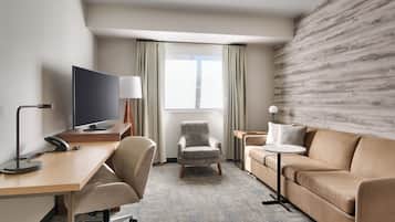 A hotel room with a desk, a television, a chair, a sofa, and a window with curtains.