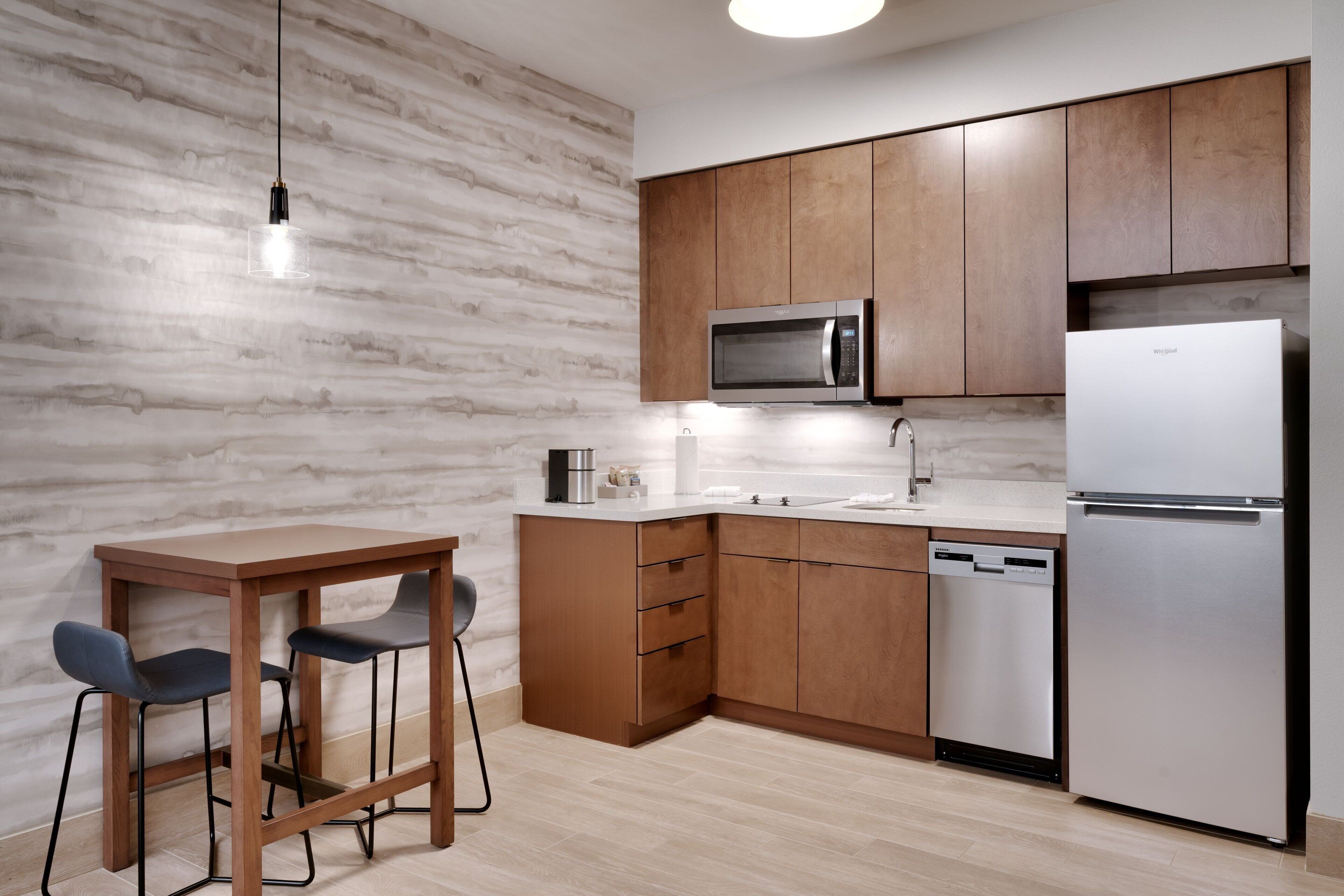 Une cuisine moderne avec des meubles en bois, un réfrigérateur en acier inoxydable, un four à micro-ondes, un lave-vaisselle et une table avec deux chaises.